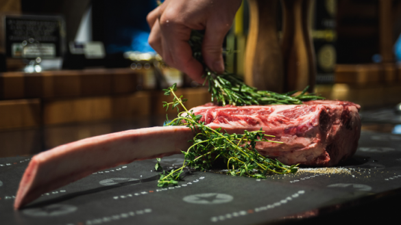 bone in rib eye steak with a close up of a hand holding rosemary