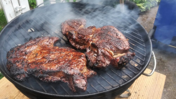 two charred delmonico steaks cooking on the grill