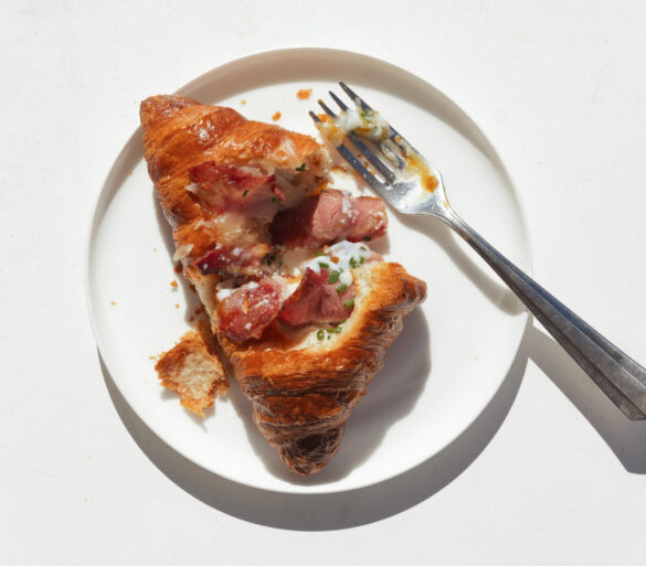 Streaky Beef Rasher & Egg Croissant on a plate being eaten with a fork.